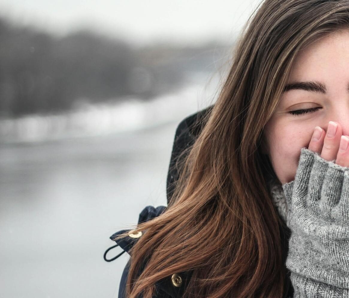 Woman in Black Hooded Down Jacket Covering Her Face With Grey Fingerless Gloves